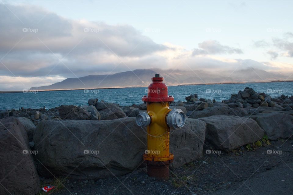 A red-and-yellow fire hydrant in Iceland near the water which creates nice contrasts.