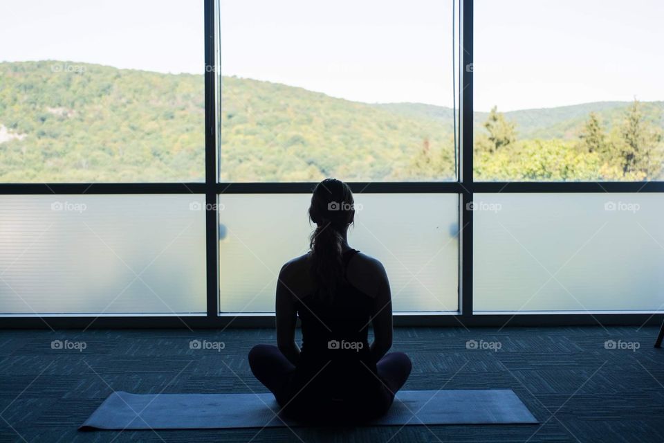 Young woman meditates before a yoga session while looking out to a beautiful landscape of mountains 