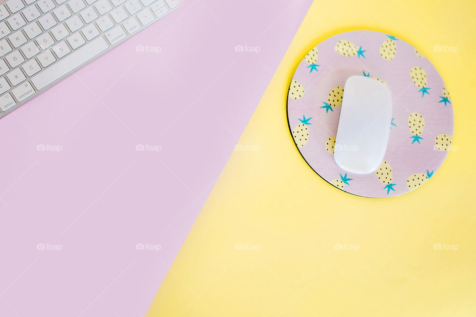 Yellow and pink desktop with keyboard, mouse and pineapple mouse pad. Fun female entrepreneur workspace concept 