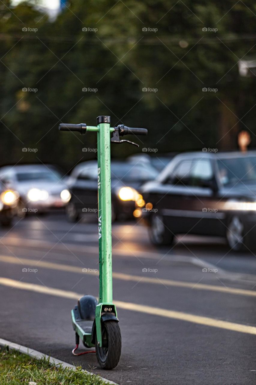 Eco friendly urban gadget. Electric scooter on the background of evening traffic.