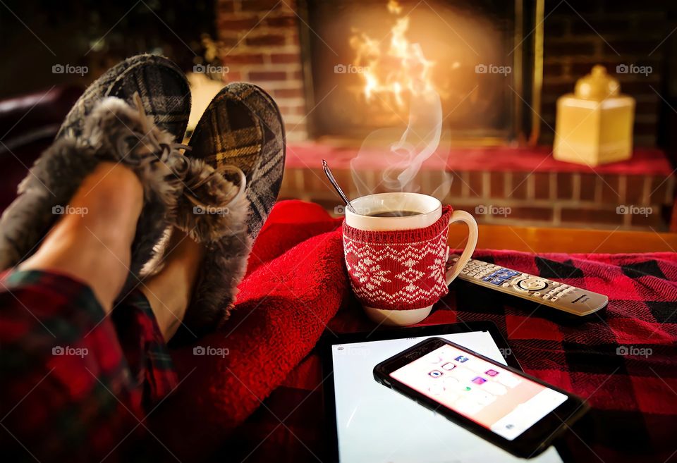 Relaxed with a cup of coffee near the fire relaxing by the hot fire with a cup of hot drink in black checkered shoes, with iPad and TV remote control.