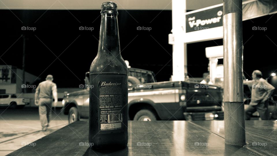 Caminhão em posto de combustível. Homens e garrafas de cerveja na mesa.