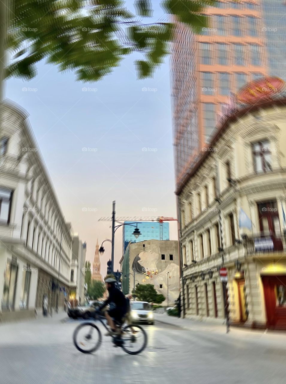 Sunset serenity in the city—cyclist passing through a blend of modern art, historic architecture, and urban life. A perfect moment captured in vibrant colors and motion.
