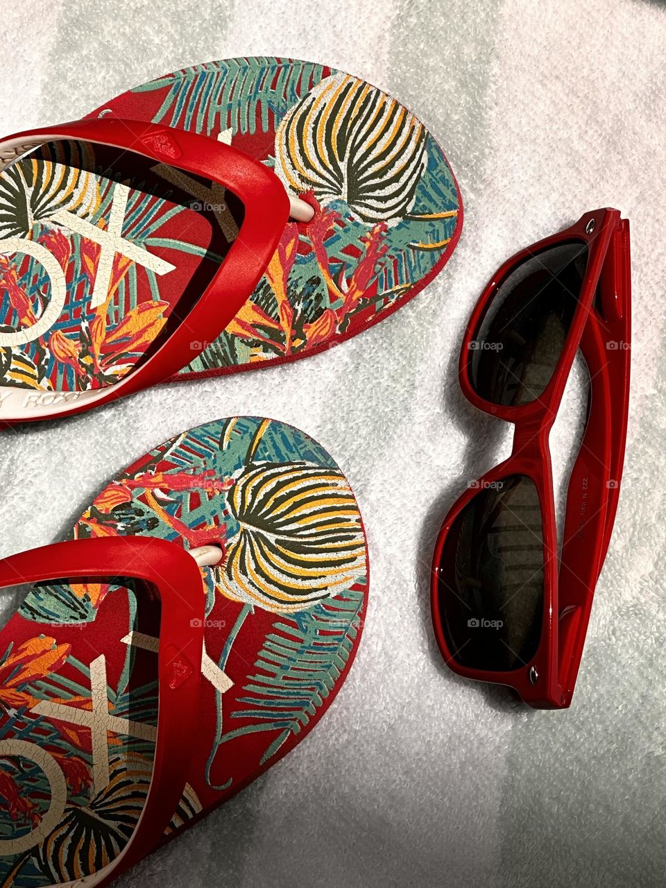 Red tropical pattern Roxy flip flops with lipstick red sunglasses on an aqua and white striped towel