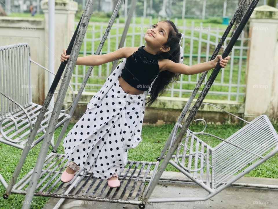 Beautiful girl swinging on outdoor swing by wearing black and white polka dot dress and having fun 