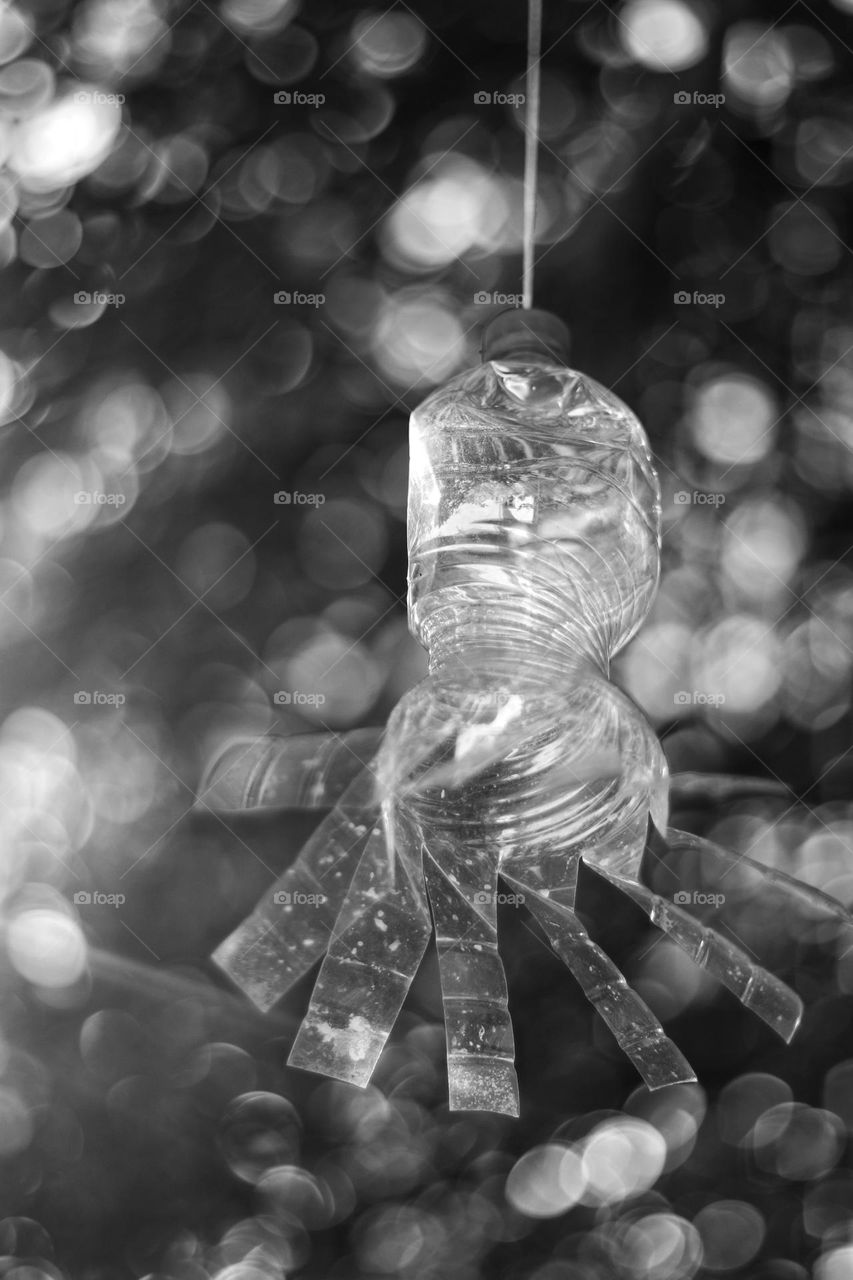 Black and white photo of a wind chime made from a plastic bottle hanging in a tree