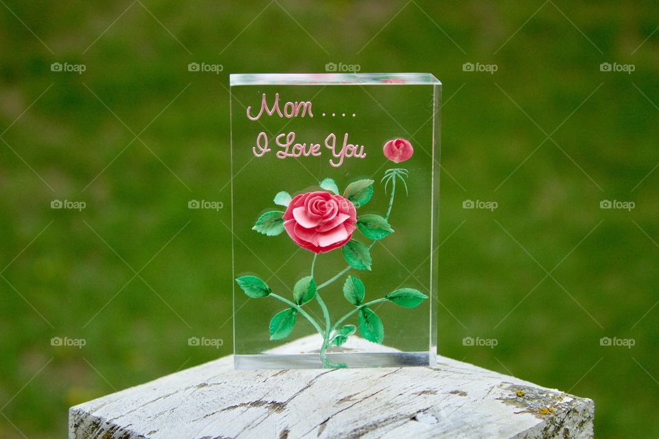 “Mom....I Love You” plaque outdoors on a weathered white post against a blurred grass background (landscape)