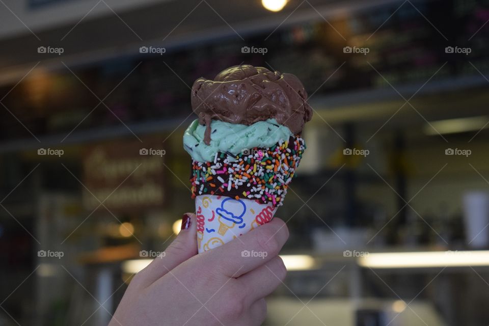 Hands holding ice cream. Mint chocolate chip and chocolate in a chocolate dipped sprinkle cone