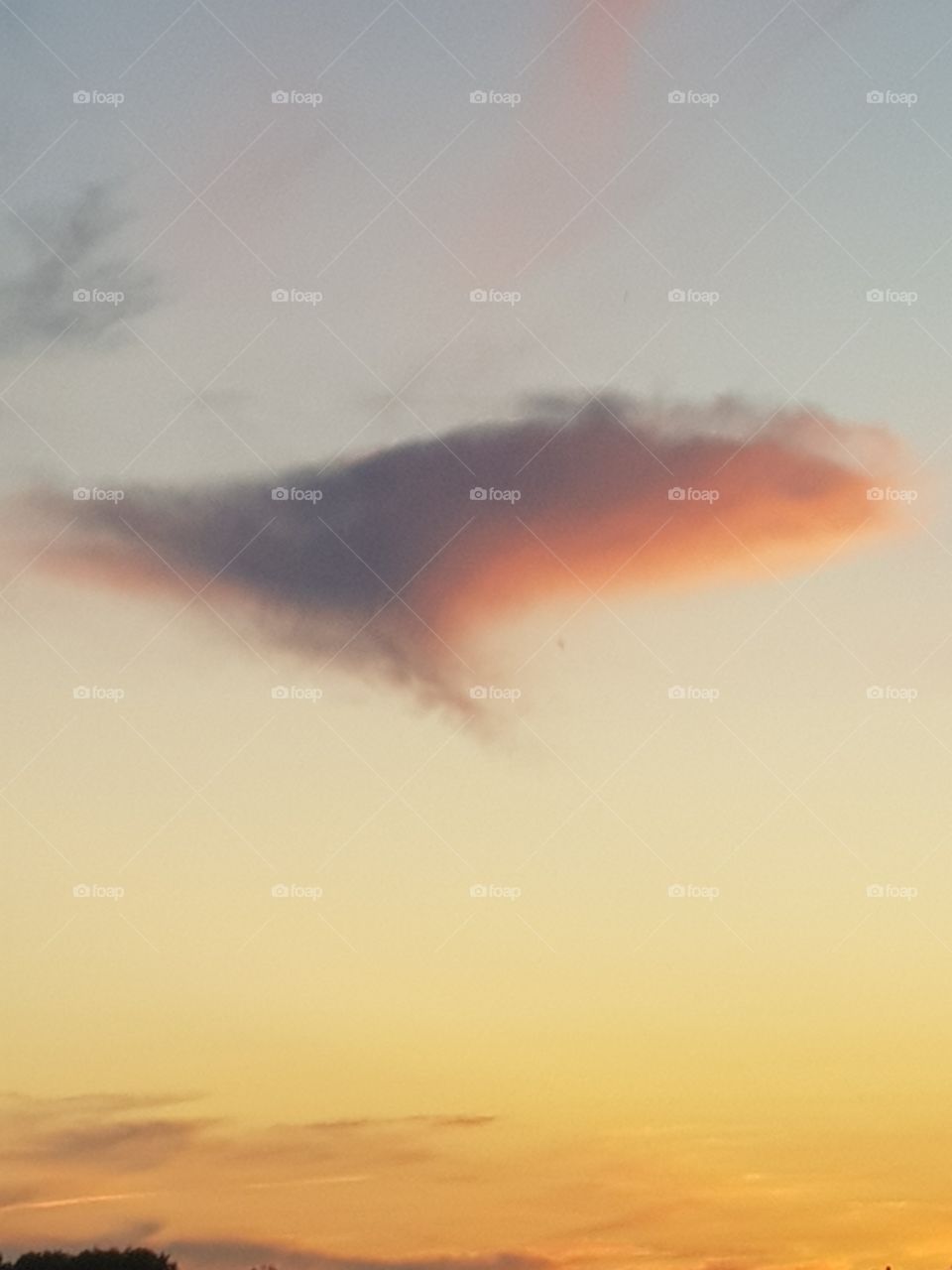 A cloud at sunset with beautiful yellow and gray sky. The cloud hangs over a lake.