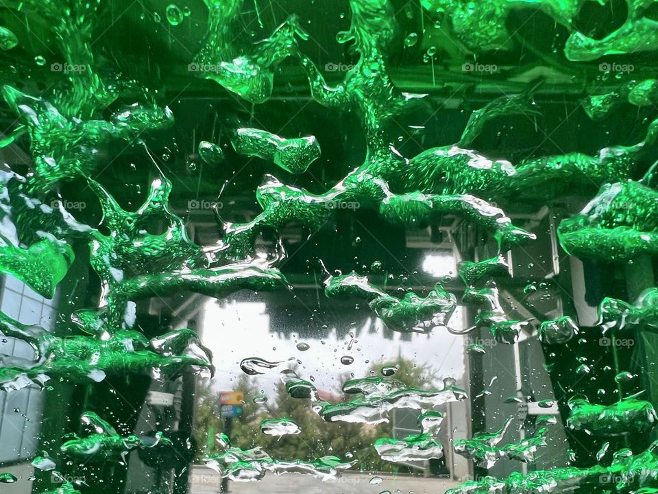 Beads of water turn neon green under the color light of a drive through car wash, distorting the view of the exit 