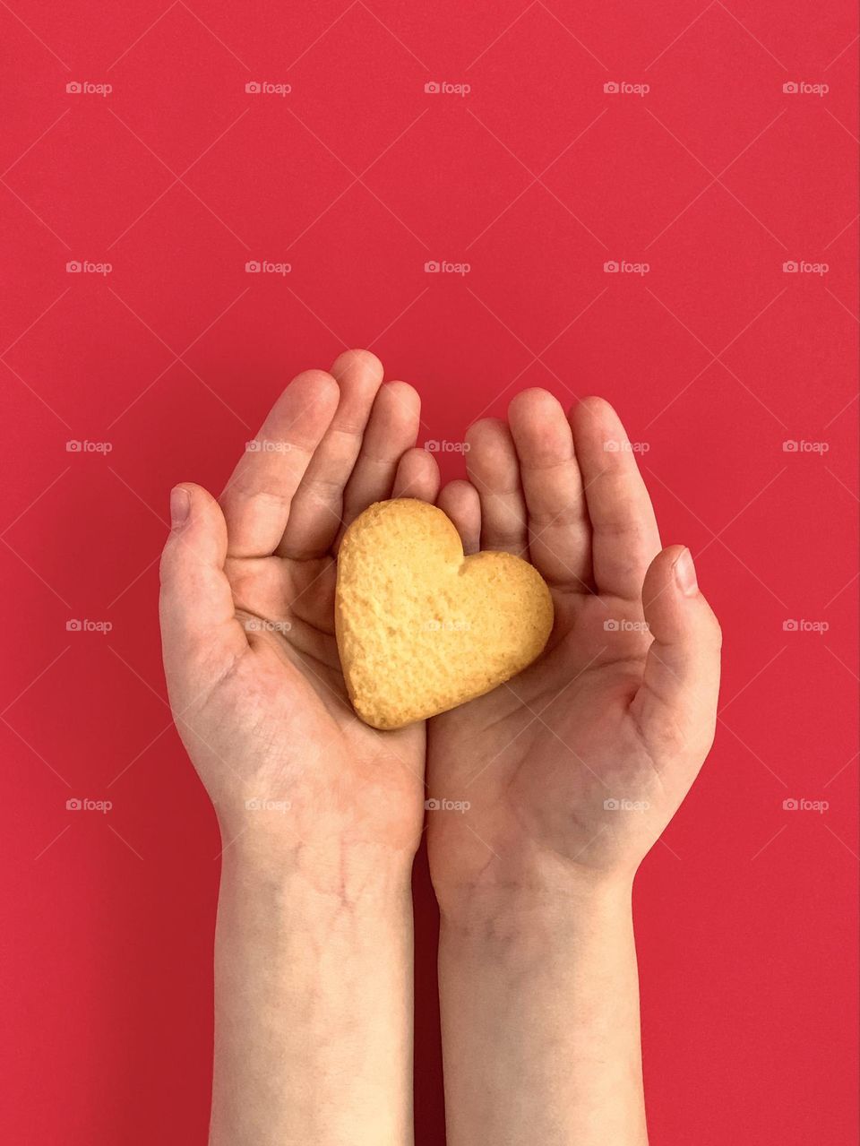 Cookie in shape of a heart in child’s hands, red background