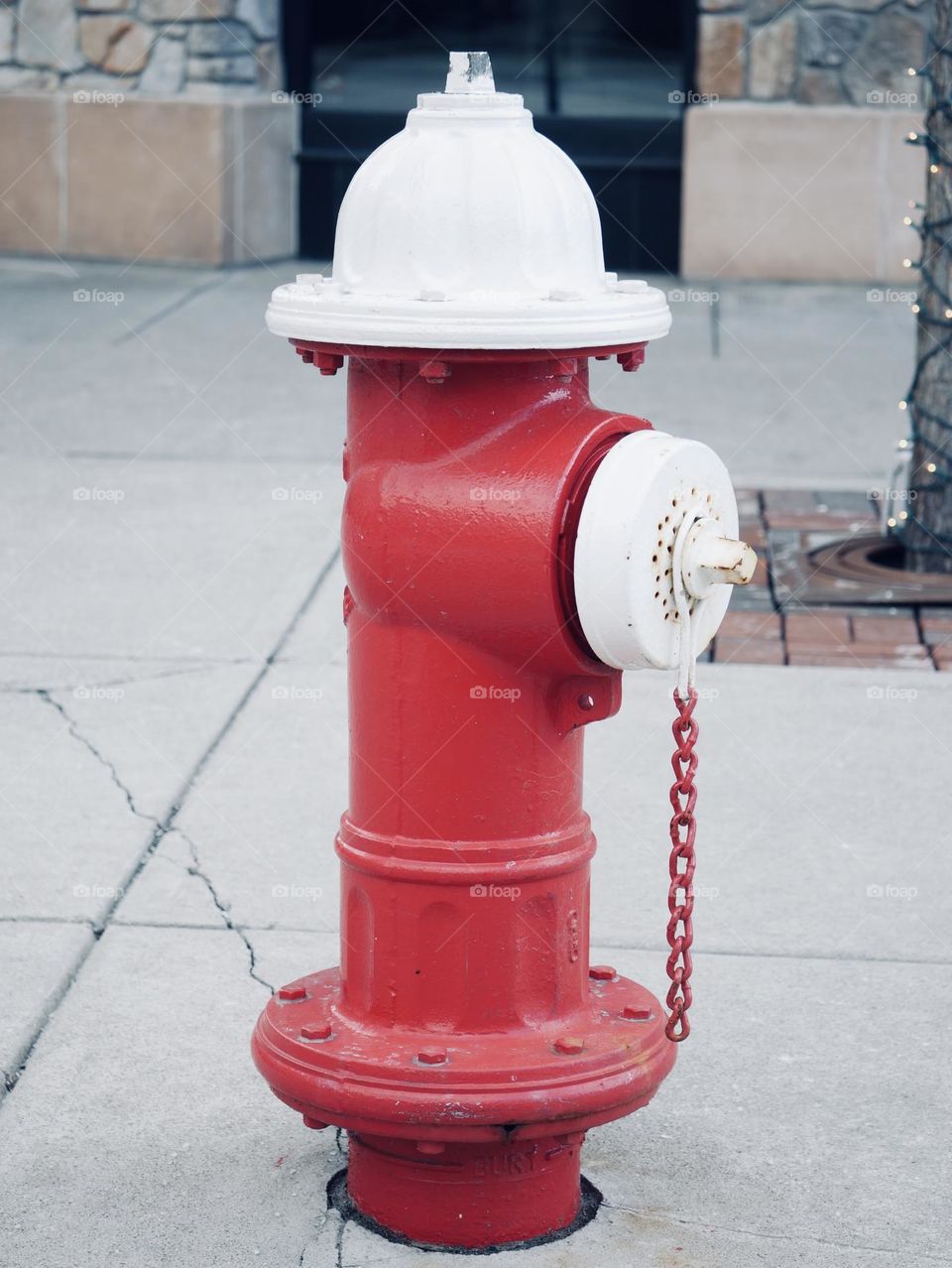 A fire hydrant on the curb, outside of a local city mall. It’s red and white. 