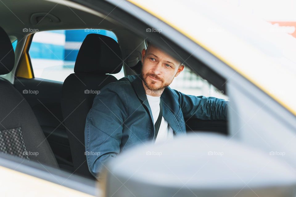 Friendly smiling bearded man taxi driver wearing blue suit inside yellow car