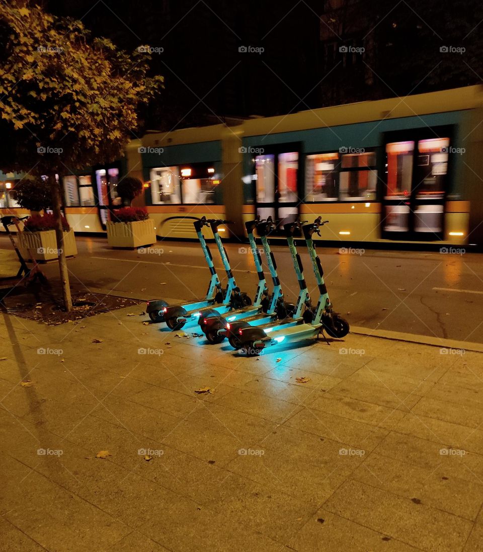 Scooters in the city / Scooters parked on the City street / Moving tram behind scooters / Night time photo of scooters in the capital of Bulgaria, Sofia