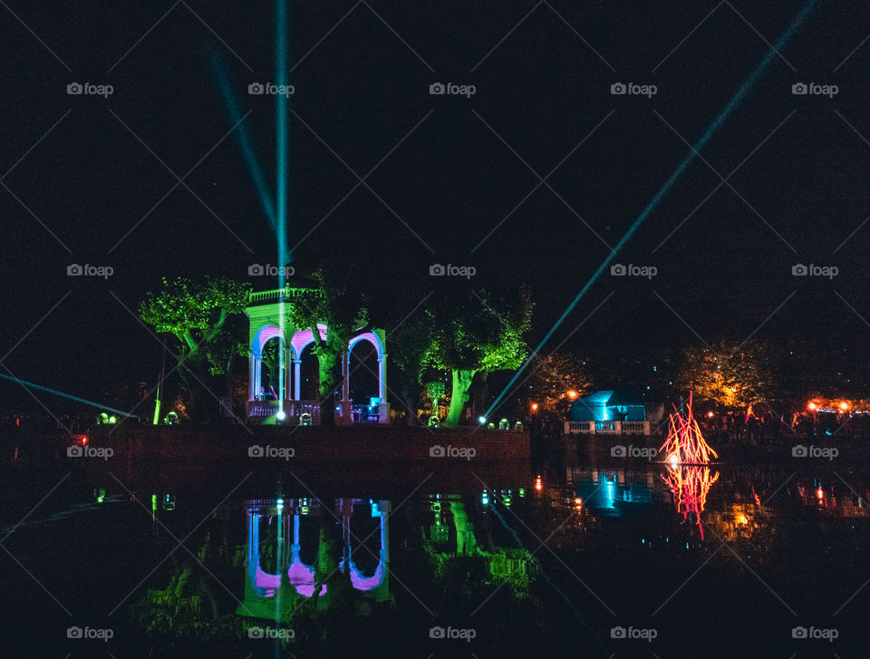 Night view of an illuminated bandstand with a lasershow on a pond during a light festival.