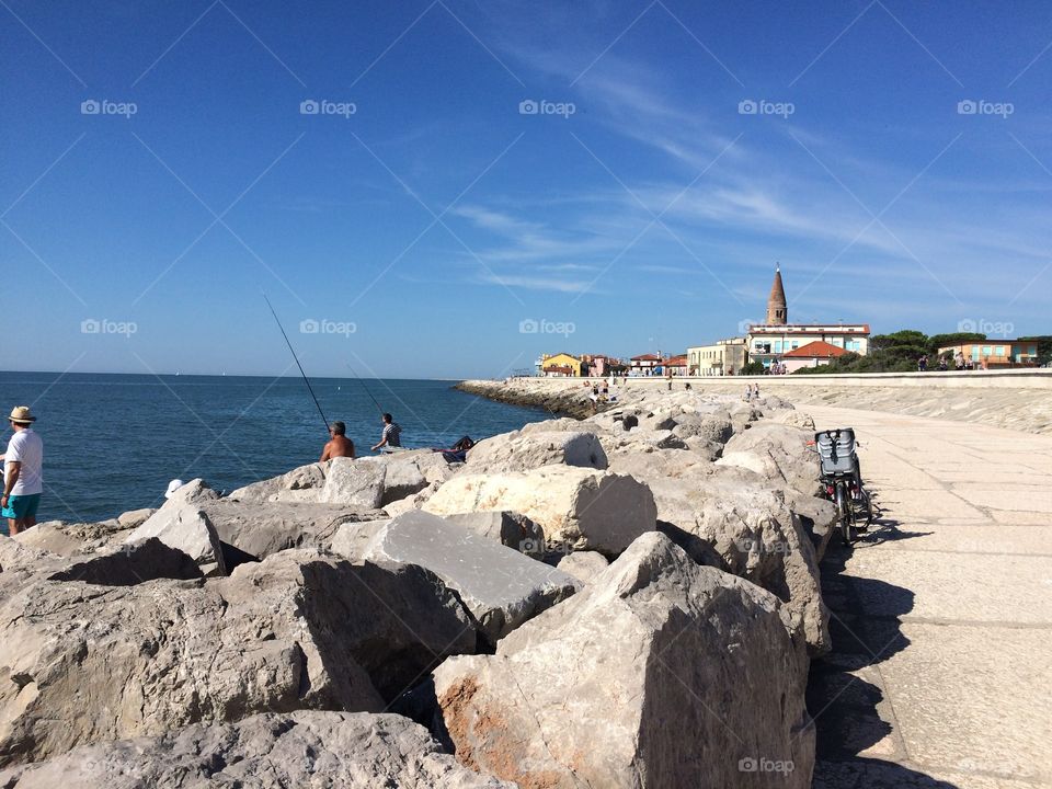 a panoramic view of caorle venice italy seafront city rock with fishermen at work