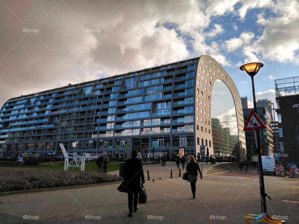 Exterior of the Markthal Rotterdam. blue sky with clouds and the reflection of the environment on the mirrored exterior of the market, there is also a man who seems to be going to work.