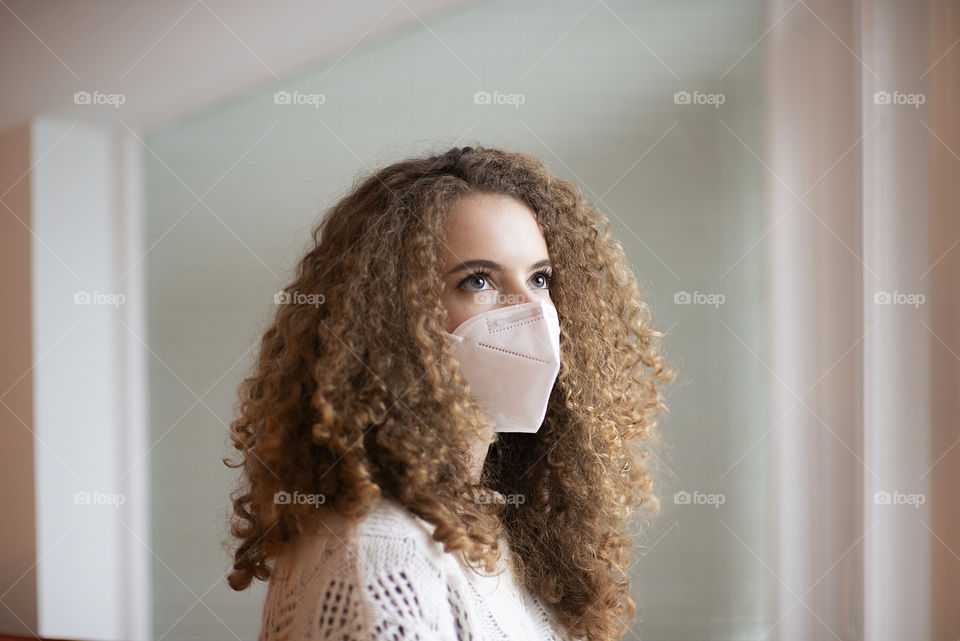 Portrait of young woman with curly hair and sad eyes in white color medical protective face mask