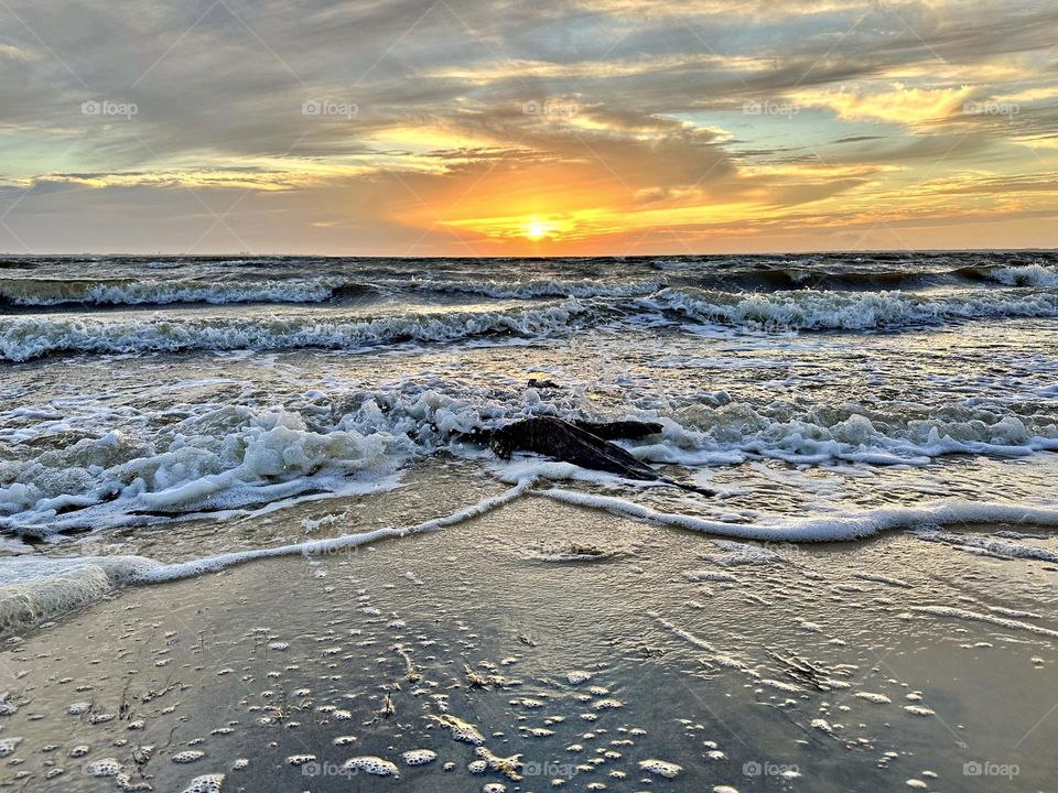 A breathtaking and radiant sunset which colors the waves iridescent, often towers and collides the shore with great force. The impact of the waves and foam against the coastline created a stunning display of energy and motion