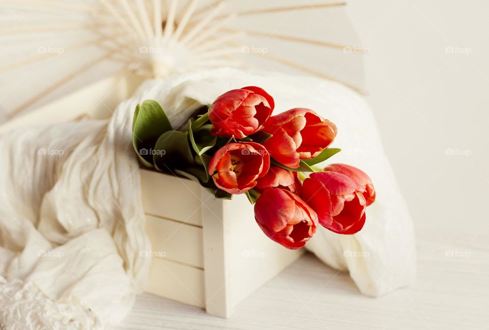 Warm toned red tulips in wooden crate with paper parasol
