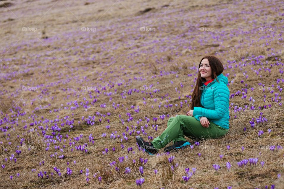 Young woman smiling and being happy while on a hike in nature, in springtime, surrounded by crocus flowers.