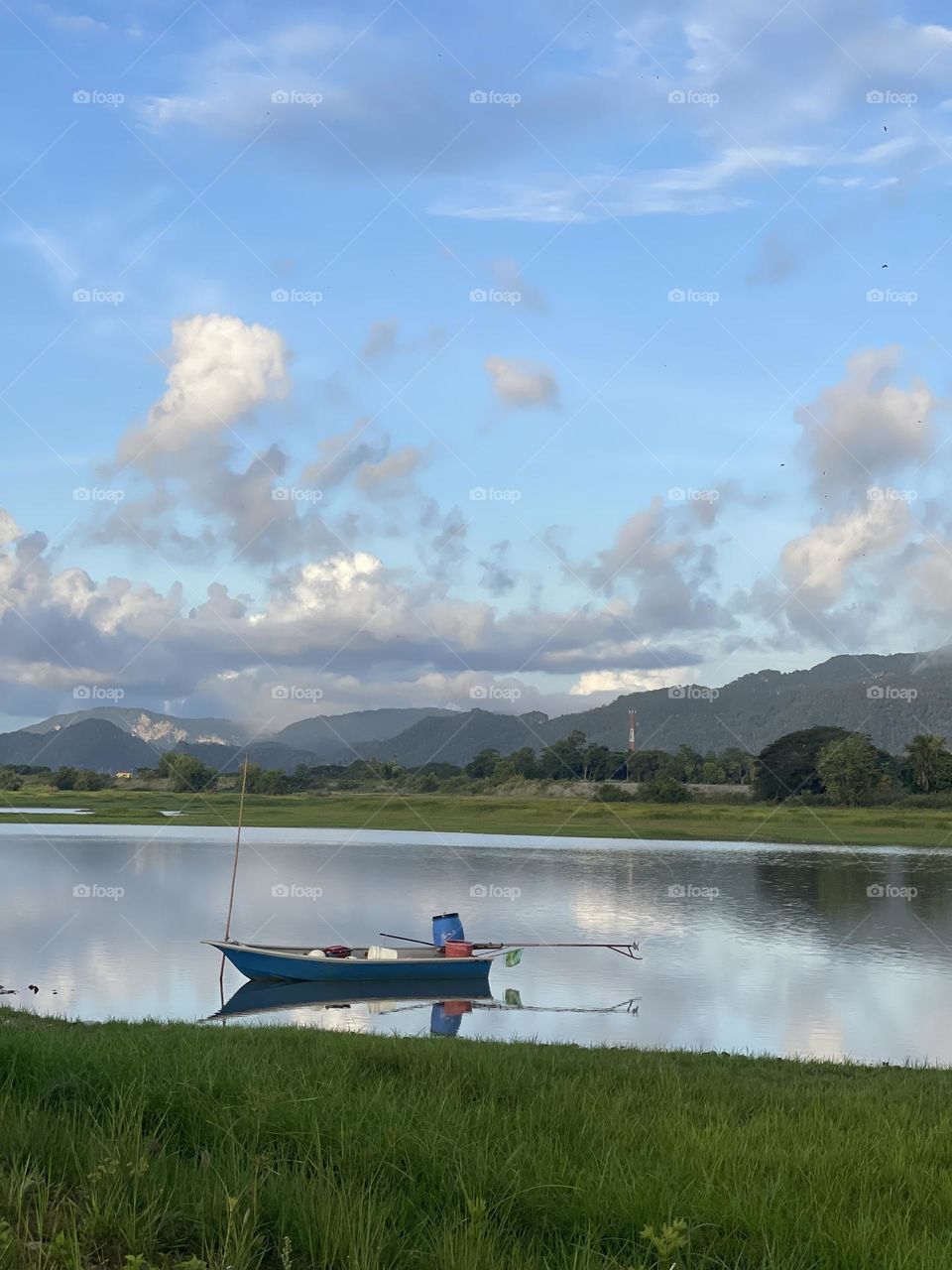 A lonely boat in the water, with beautiful scenery of mountains, clouds and sky