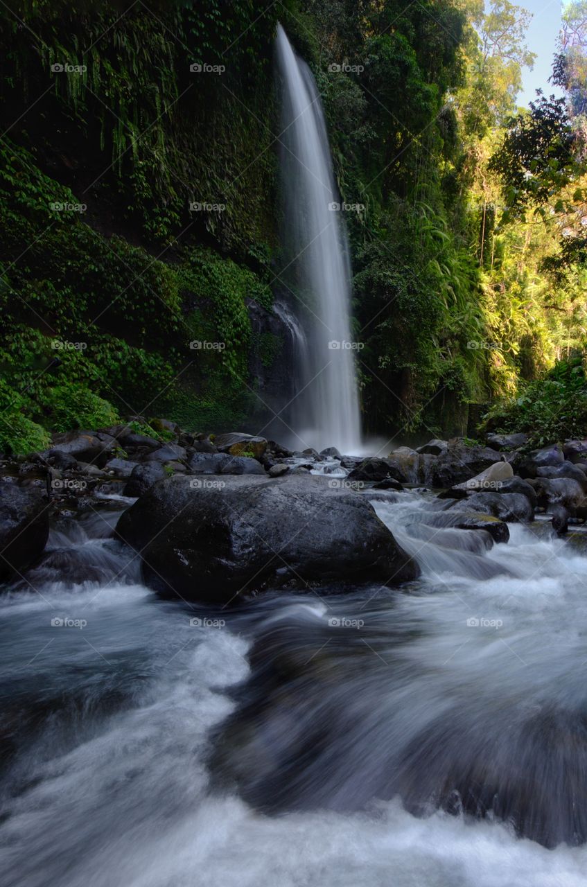 Layered water flows with cool air and green scenery are attractions that you can enjoy when you visit Sendeng Gile waterfall in Lombok, Indonesia. Motion blur and soft focus due to Long Exposure Shot.