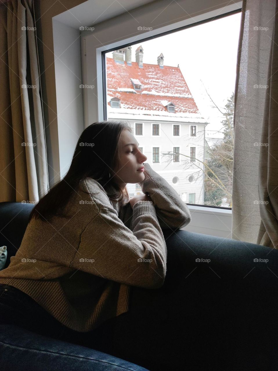 A portrait photo of a girl sitting on a sofa in front of a window in the winter