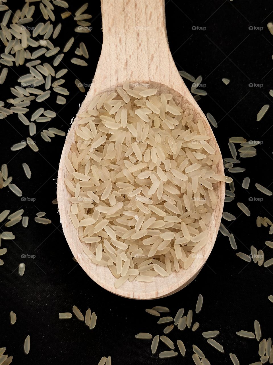wooden spoon with grains of rice on a black background with grains of rice