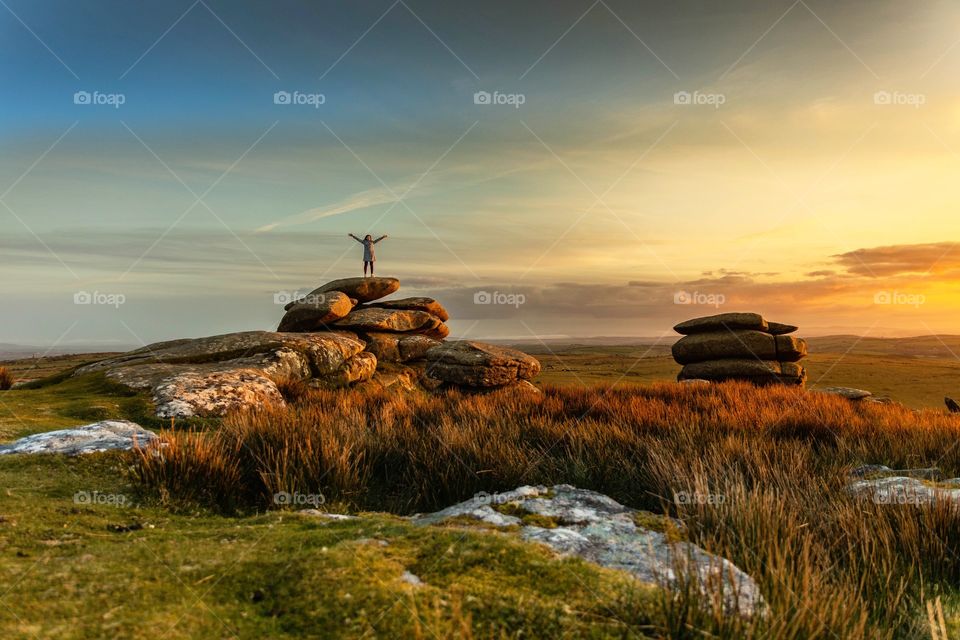 Cheesewring rocks on Bodmin Moor with a person celebrating their climb to the top of the hill in Cornwall, England.