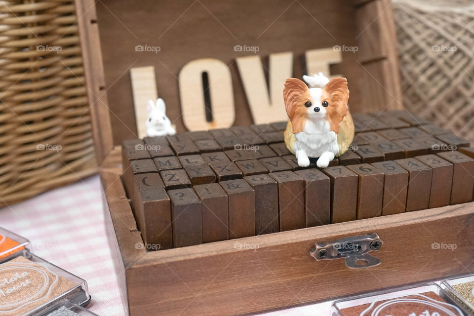 cute dog miniature. Continental toy spaniel papillon dog breed plastic toy is sitting on the alphabet wooden stamp with abstract blur wooden letter LOVE on the background. Vintage. Dog lover concept.