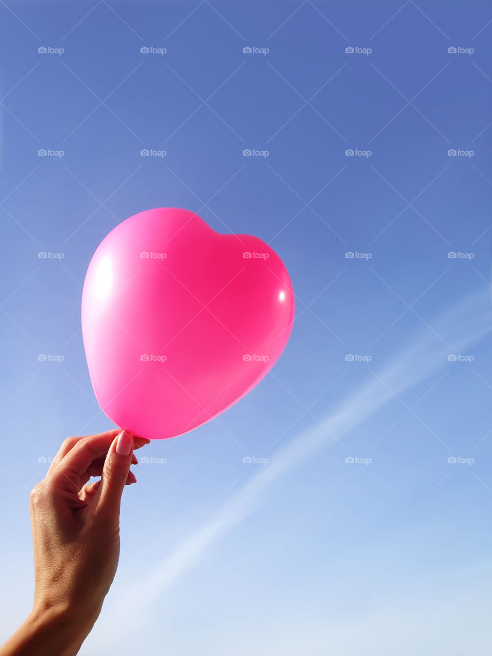 Pink party heart shaped balloon in woman hand on blue sky background 