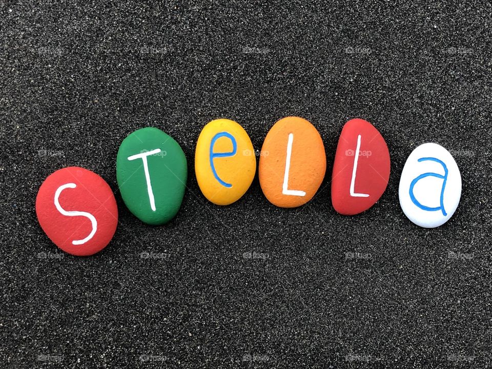 Stella, feminine given name with a multi colored painted stone letters over black volcanic sand
