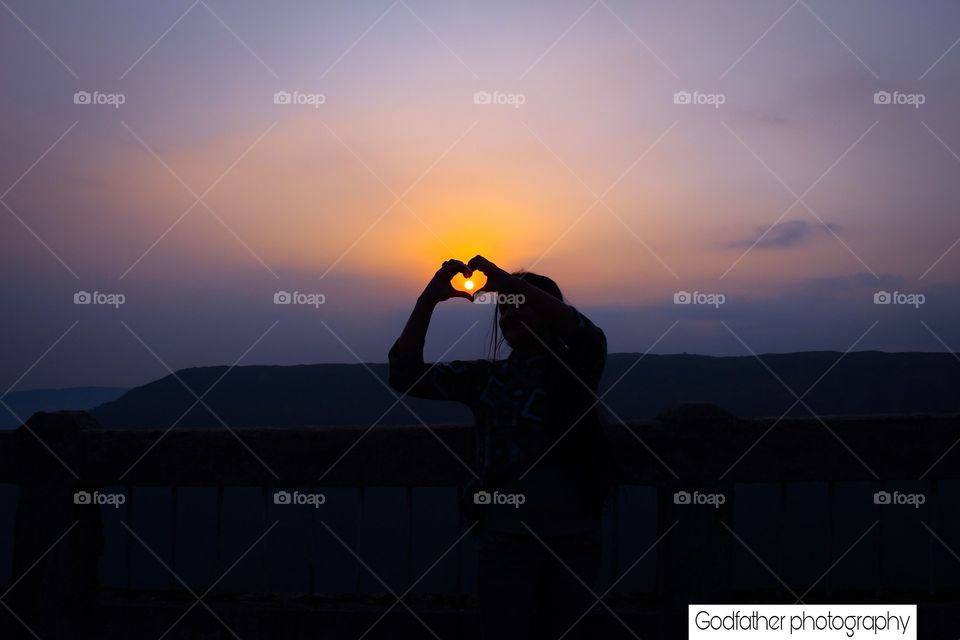 This photo is taken on the top of a mountain in Shillong. It's a sunset picture where the sun is inside the heart shaped structure made by hand.