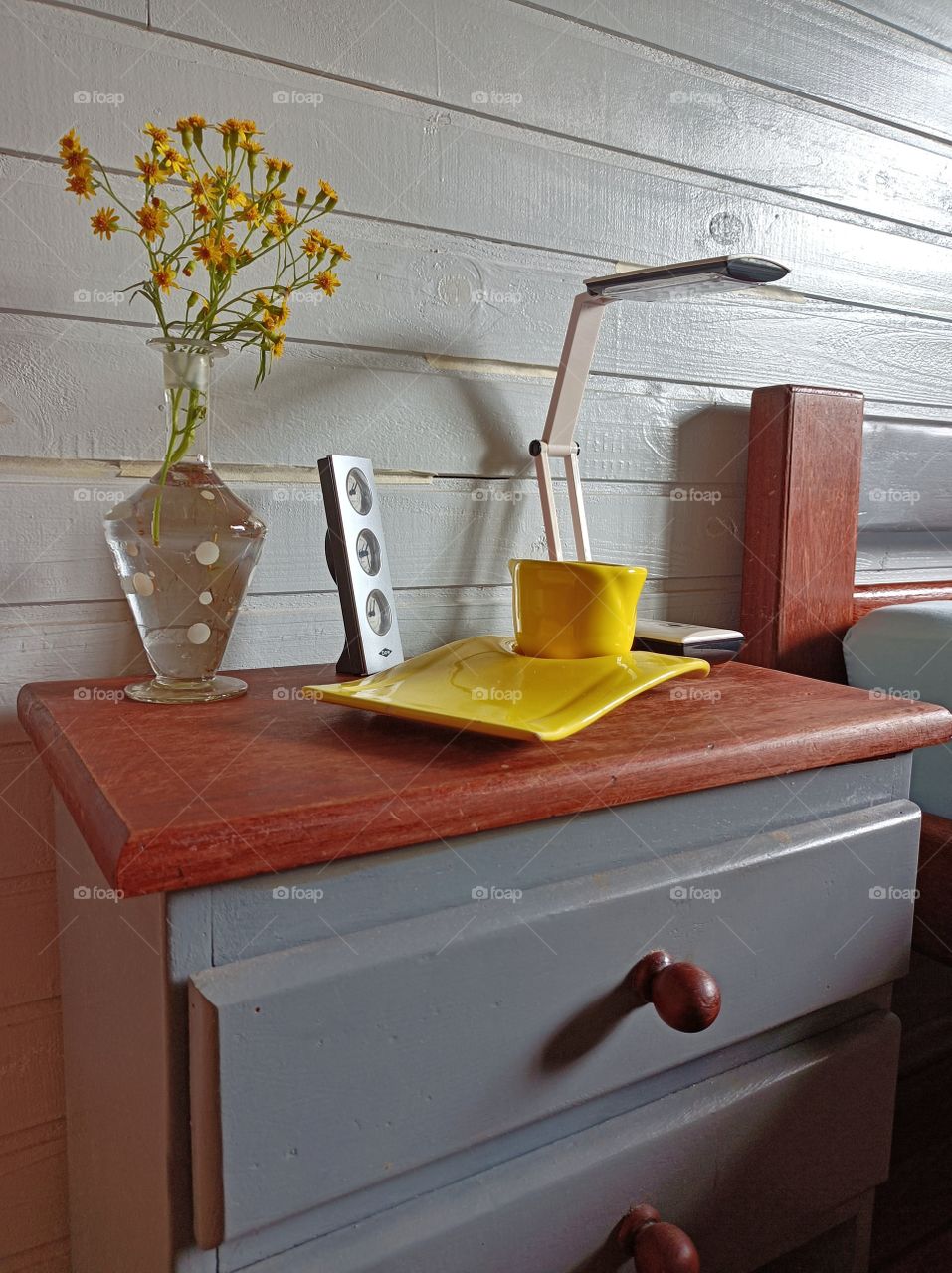 Gray bedside table and yellow cup with vase and yellow flowers