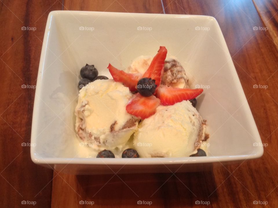 A photo of Vanilla ice cream with strawberries and blueberries. 