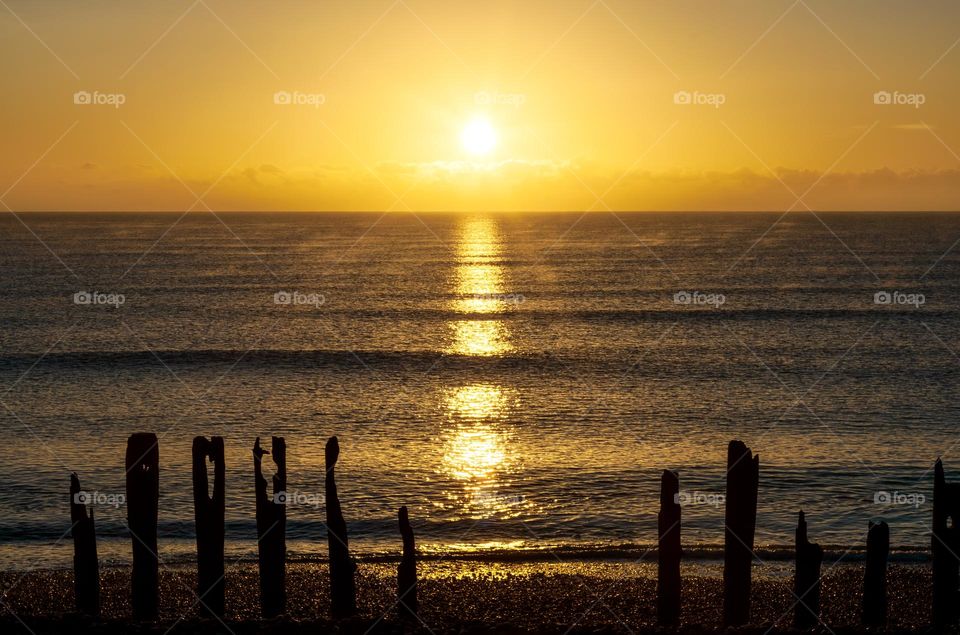 The sun has recently risen over the English Channel and wooden sea defences at Winchelsea Beach UK 