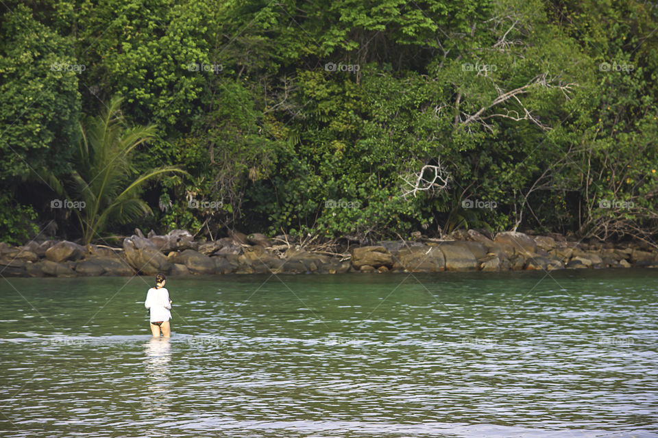 Woman walking in the sea Background trees and rocks