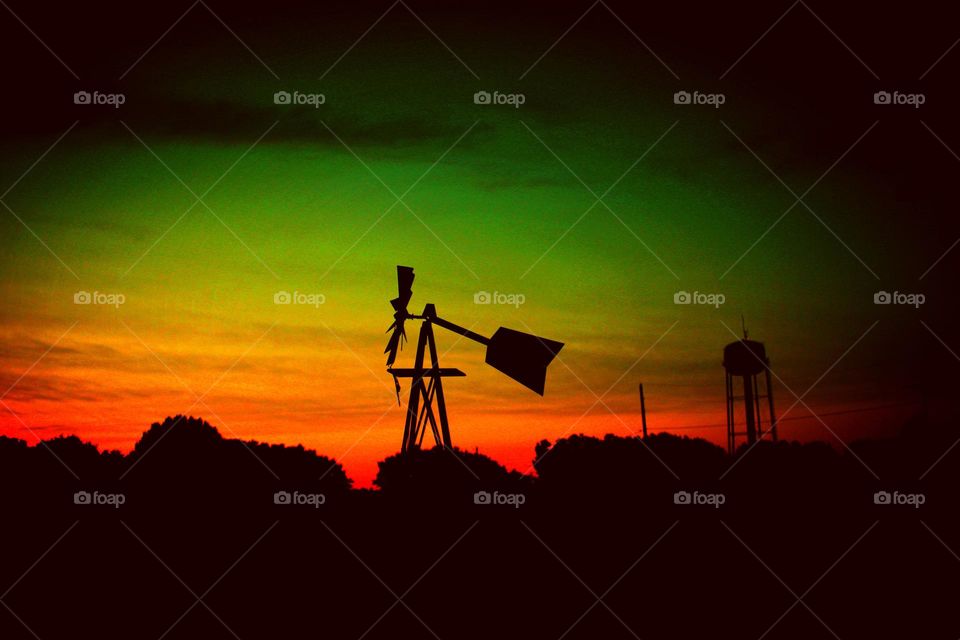 early morning sunrise silhouettes a windmill and a water tower in the background