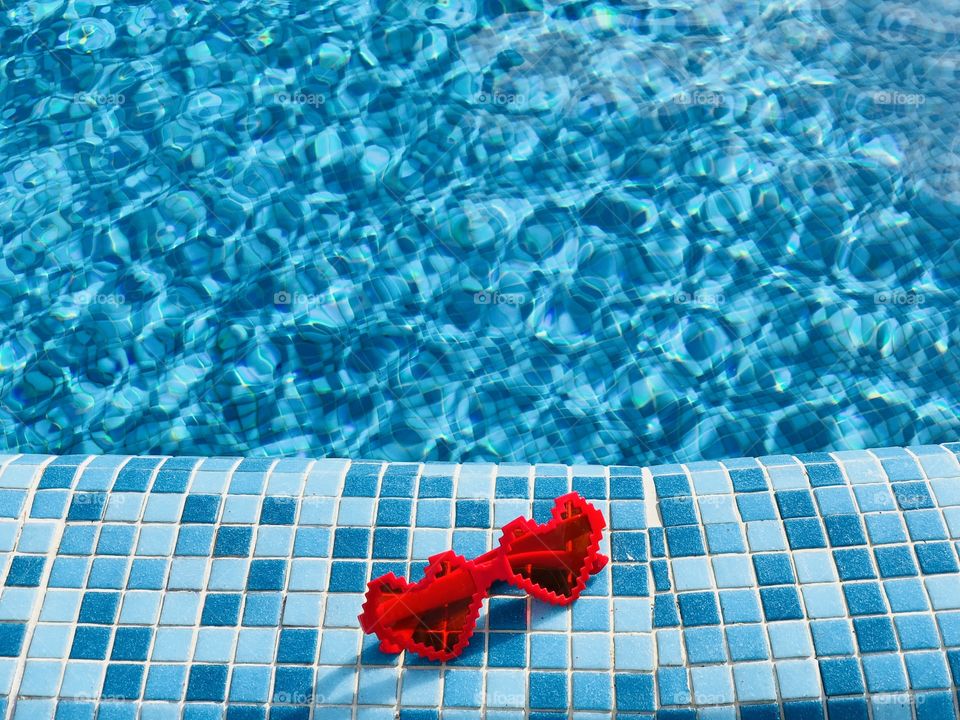 Heart shaped sunglasses on the edge of a pool with turquoise water