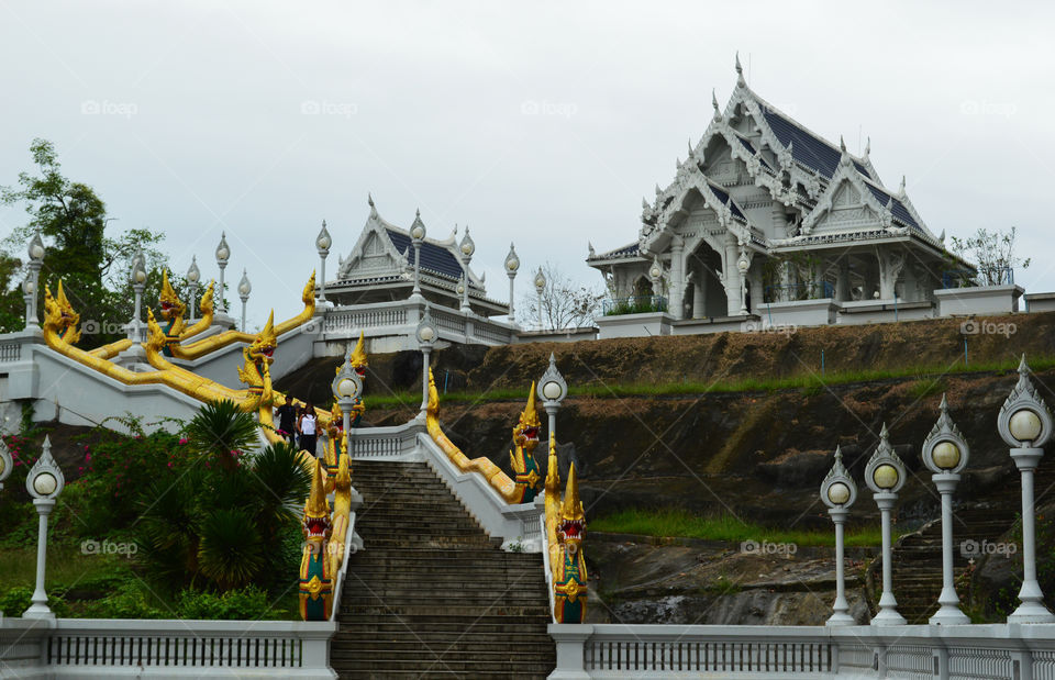 Big white Buddhist temple on top of the hill with golden stairs leading to it