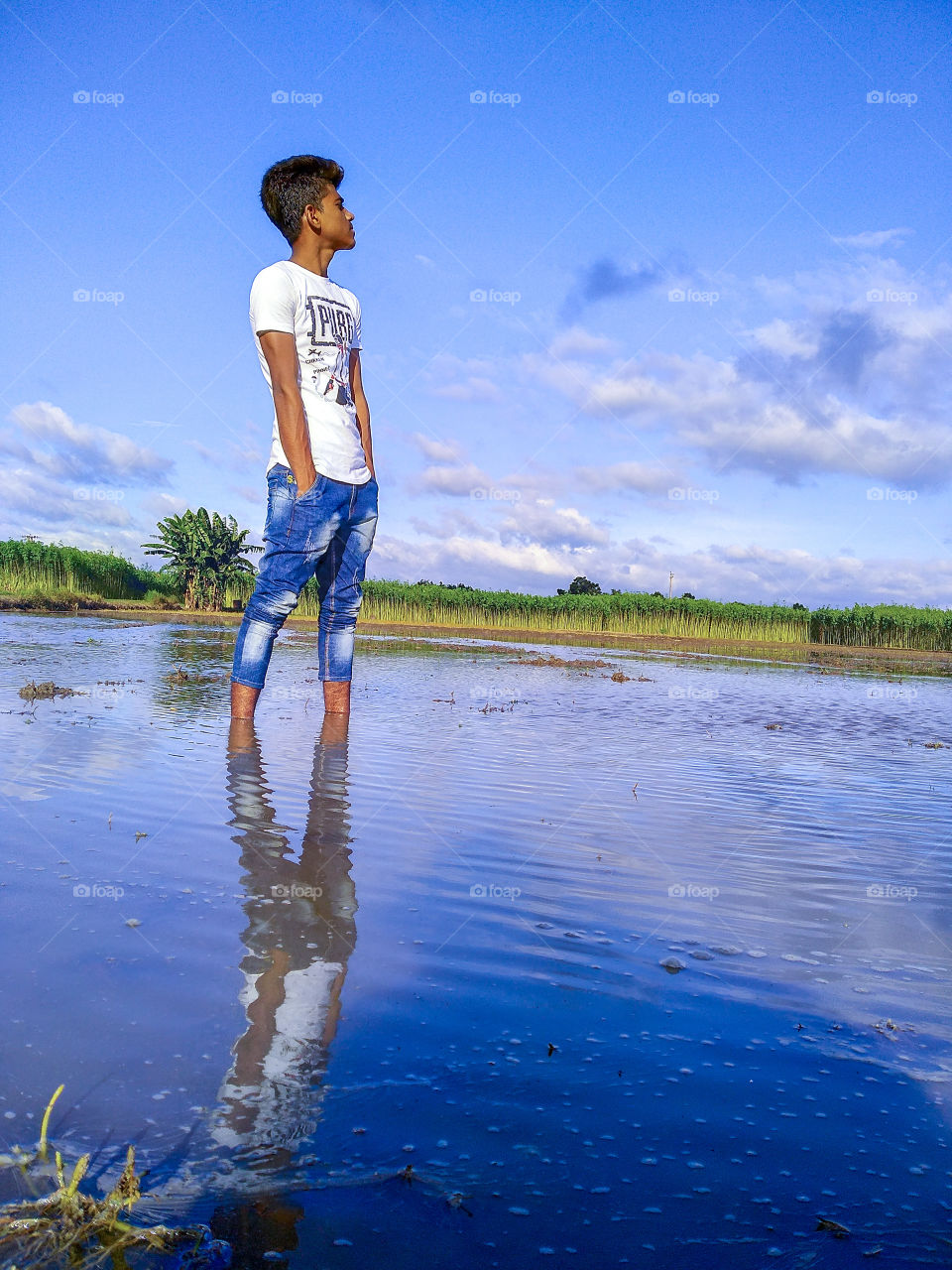 A boy stands in water. With a beautiful blue sky background. He is watching towards the sky.