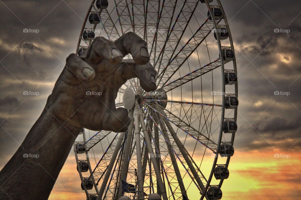 Giant's Wheel. A giant structure grabs a Ferris wheel. 
