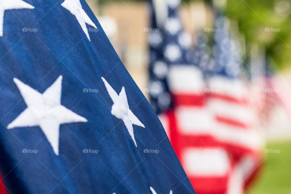 Horizontal photo of a close up of the white stars on the blue background on an American flag and several other US flags in soft focus in the background