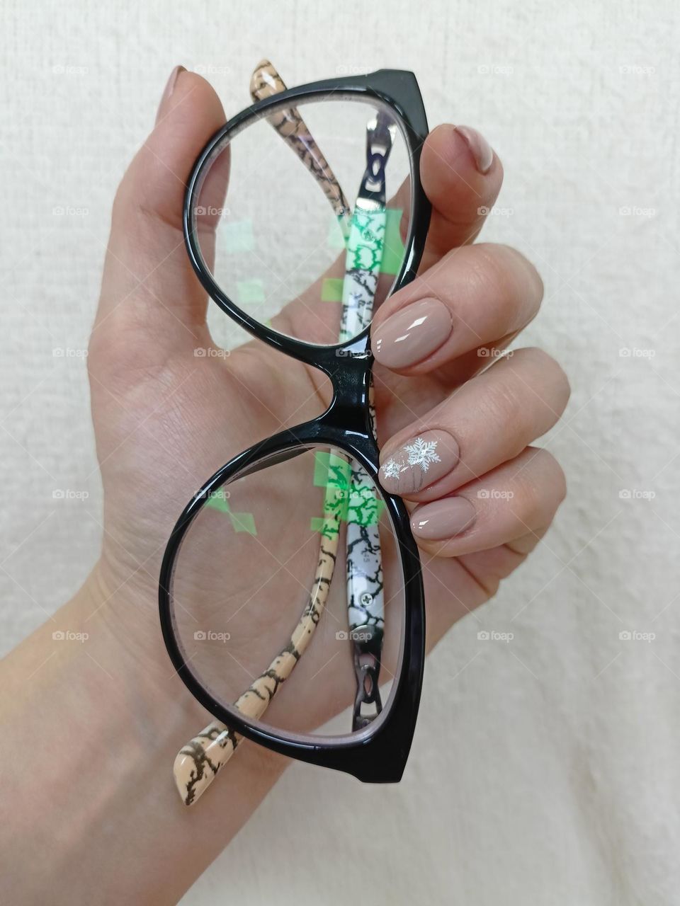 manicure on a female hand, the color of nails is coffee with milk, a white snowflake, female hands on a white background, a warm fluffy scarf, nail polish,glasses in hand, reflection in glasses glasses