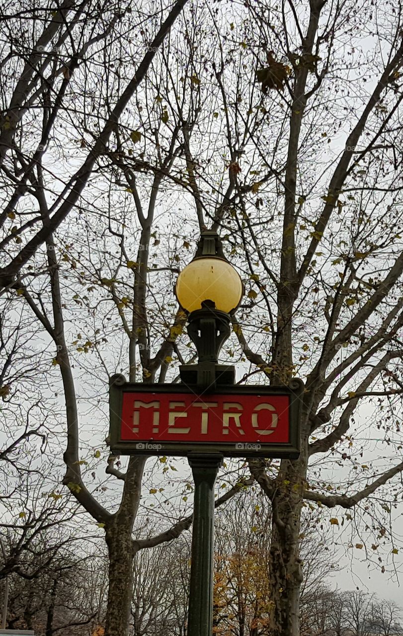 Old vintage metro sign with street lamp in Paris France with winter sky and bare tree branches behind