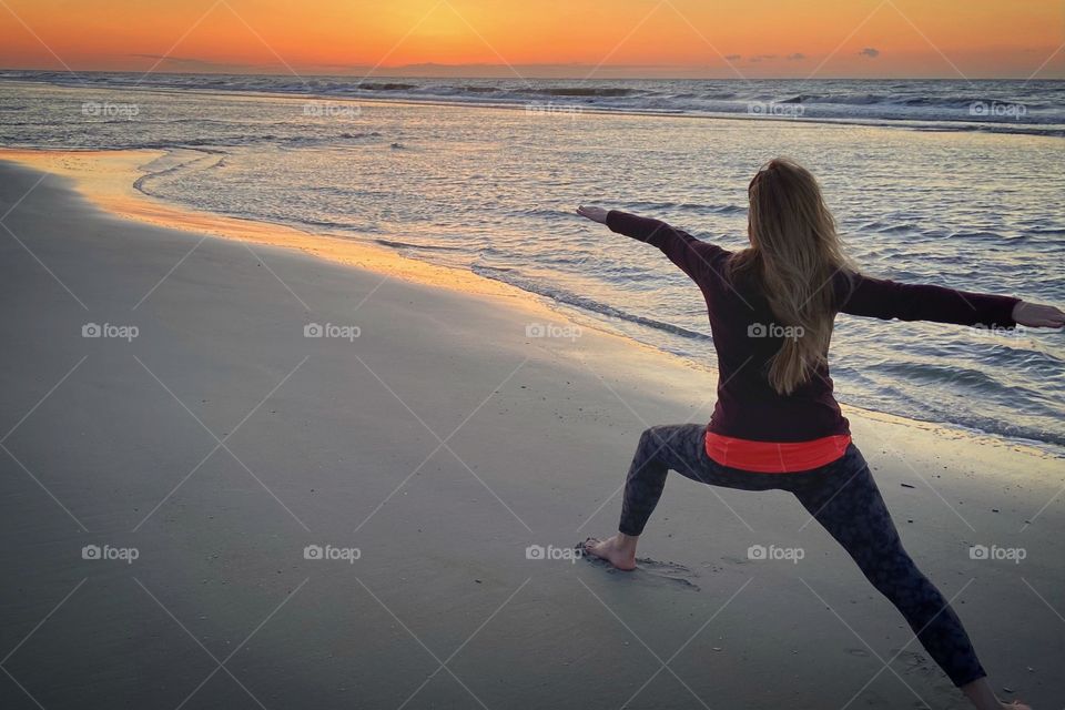 An athletic woman stands in warrior pose at sunset on a sandy beach in Hilton Head, North Carolina