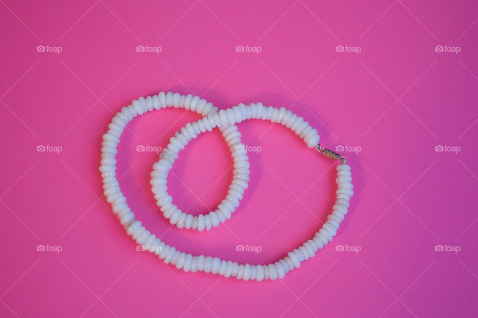Contrasting flatlay on a bright pink background with a white shell necklace 