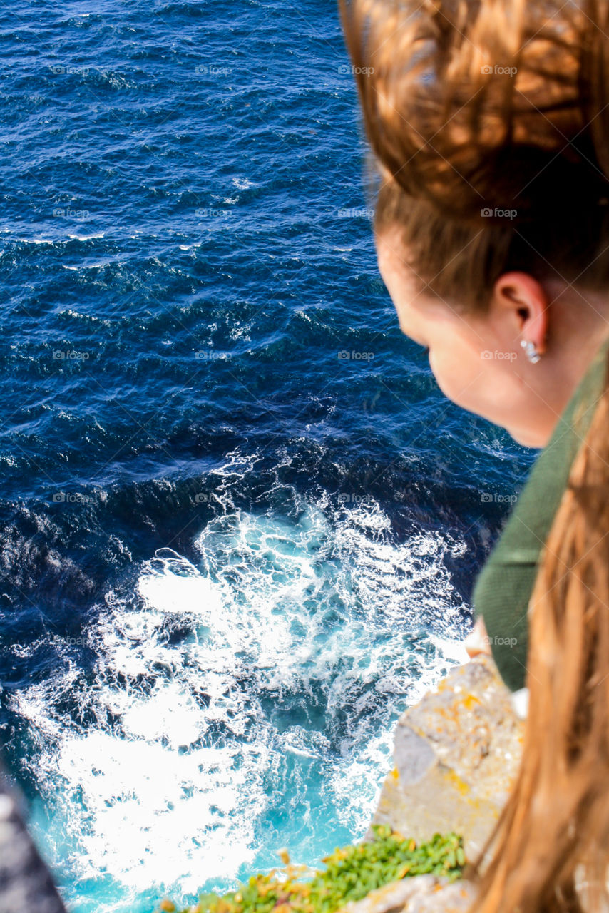 Girl looking off of a cliff into the ocean. 