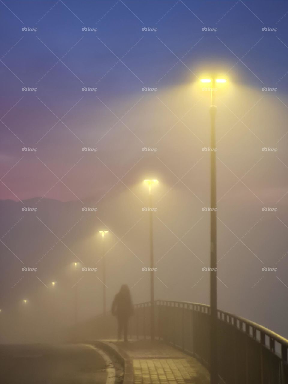 silhouette walks in the fog under the lit street lamps